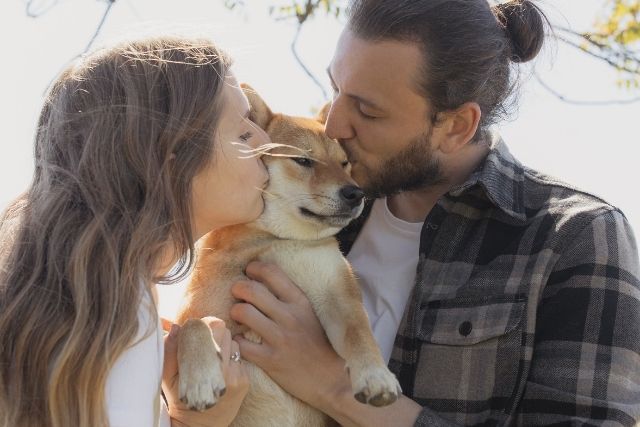 Mann und Frau (Pärchen), die ihren Hund auf die Wangen küssen - Tassenliebling Kollektion für Tierliebhaber